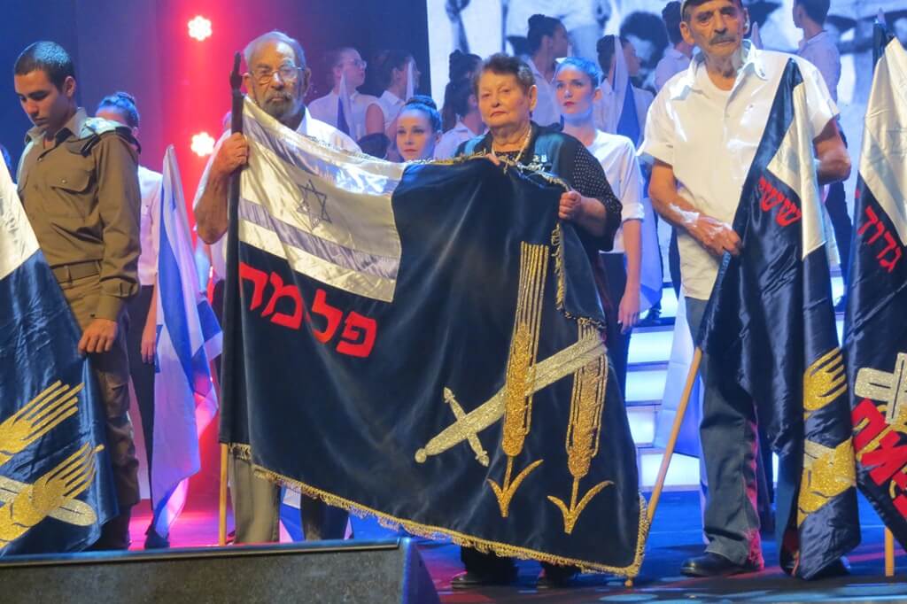 תמונה דגל הפלמ"ח מוצג לראווה בידי טובה עופר ופוצ'ו (אריה ויסלר). מימינם פסח עזריהו