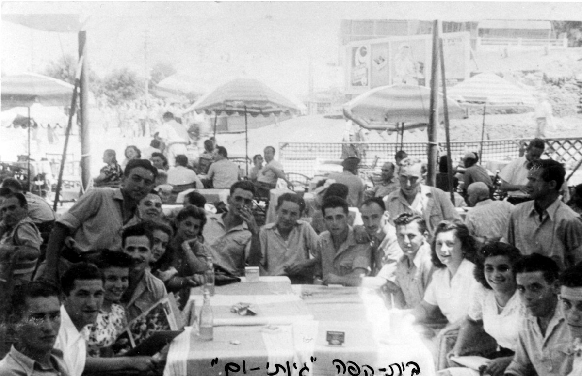 פלוגה ד', תיאור התמונה: חופשה בתל-אביב, בית קפה - "גינתי-ים". מופיעים בתמונה: בני קפלן, (?), (?), אהרון ידידיה, שמואל רוזנפלד, משה גולדפרב, ברוך יקותיאלי, עומד: יעקב נויברג. נתקבל מ: שמואל רוזנפלד: ניצה (צרפת) תמונה
